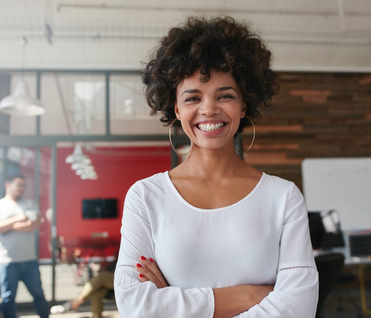 smiling-young-woman-standing-in-creative-office-PHKL7DX-scaled.jpg